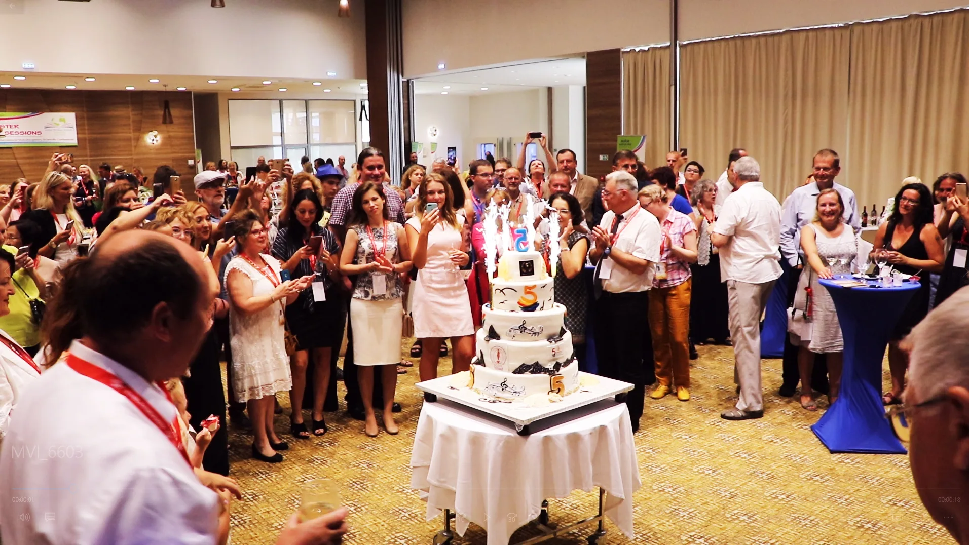 A speaker addressing conference guests beside a large cake