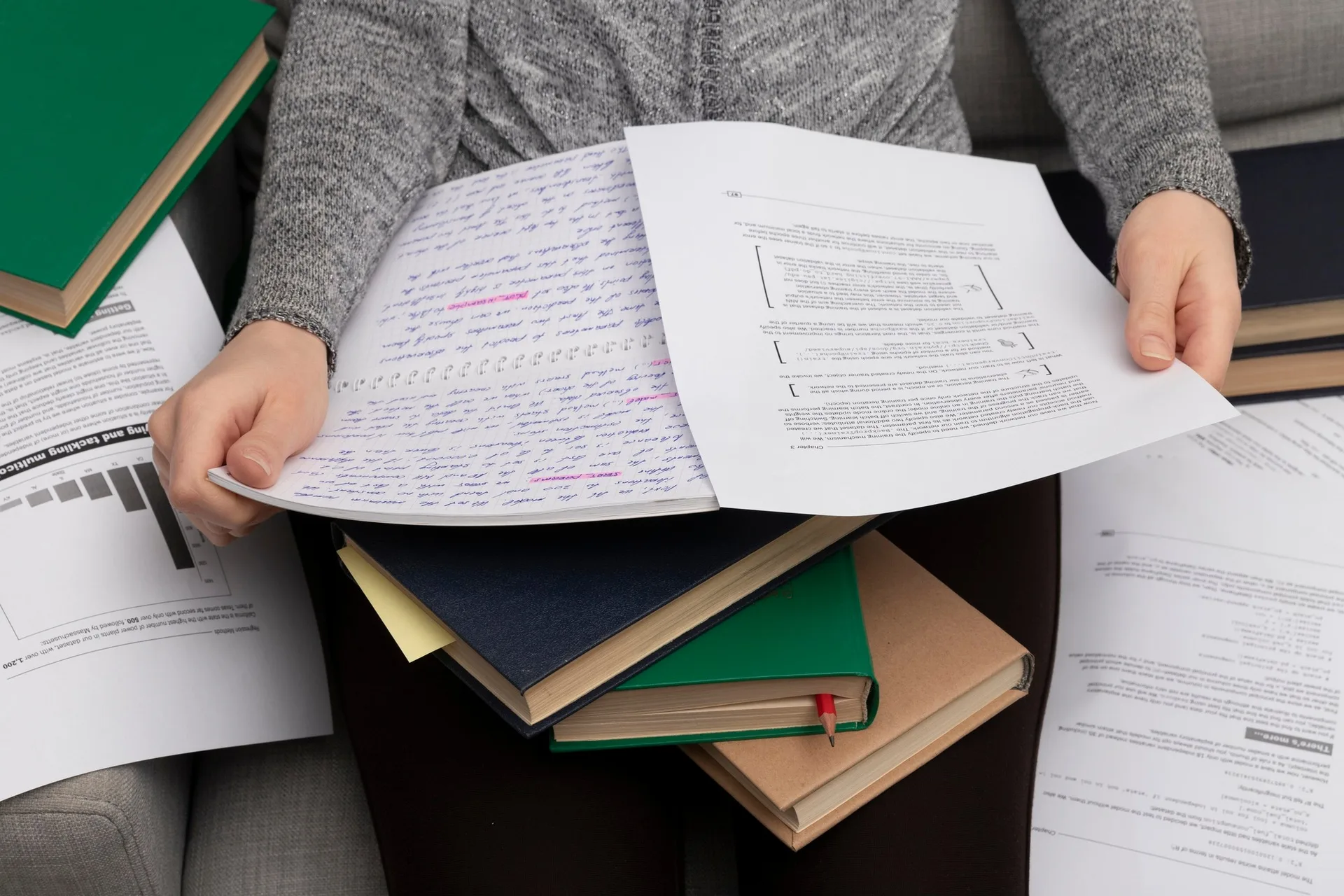 A researcher reading marked-up papers over a stack of books