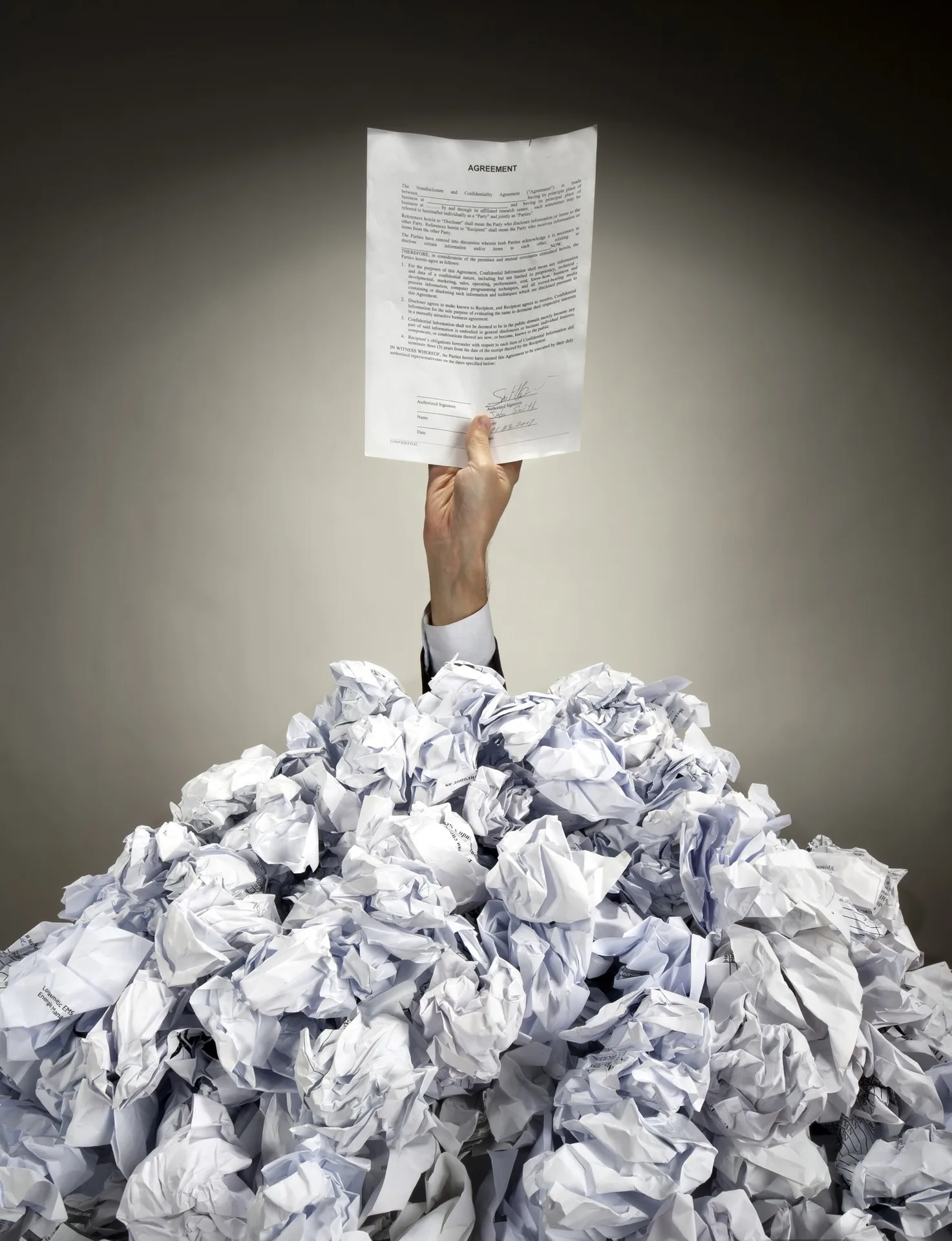 A hand holding a document above a pile of crumpled papers
