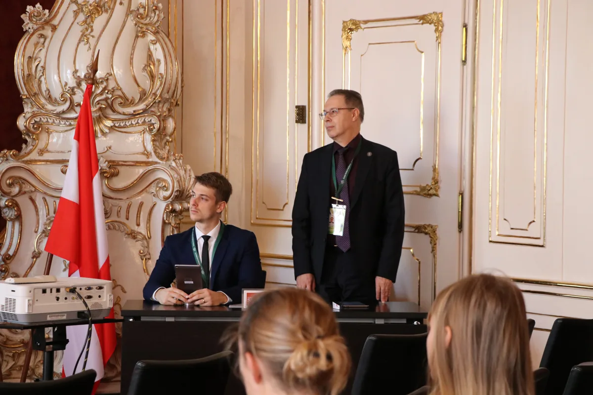 A speaker addressing delegates beside a conference panel table