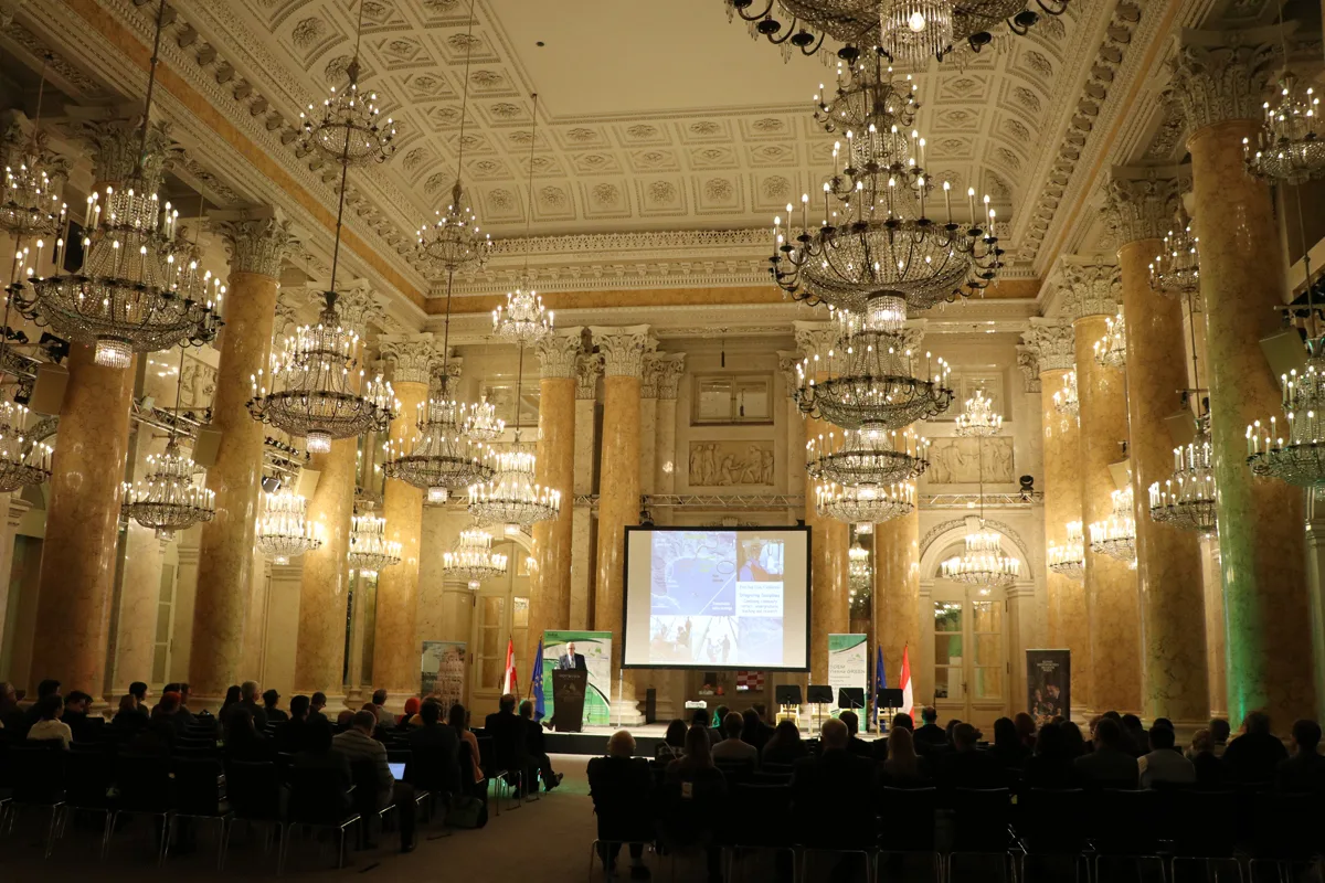 A full conference audience beneath gilded ceilings and chandeliers