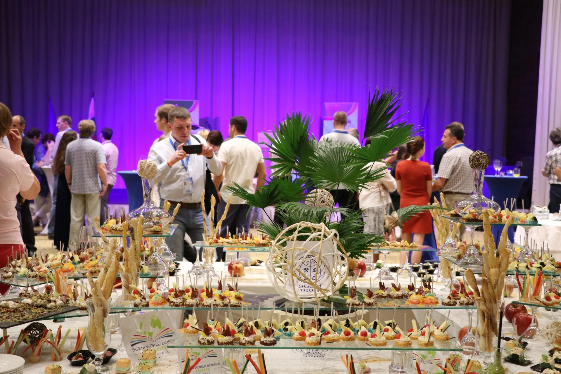 Guests mingling behind a decorated conference buffet under purple lighting
