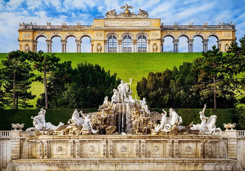 Un jardín de palacio con una fuente esculpida y un pabellón con columnas