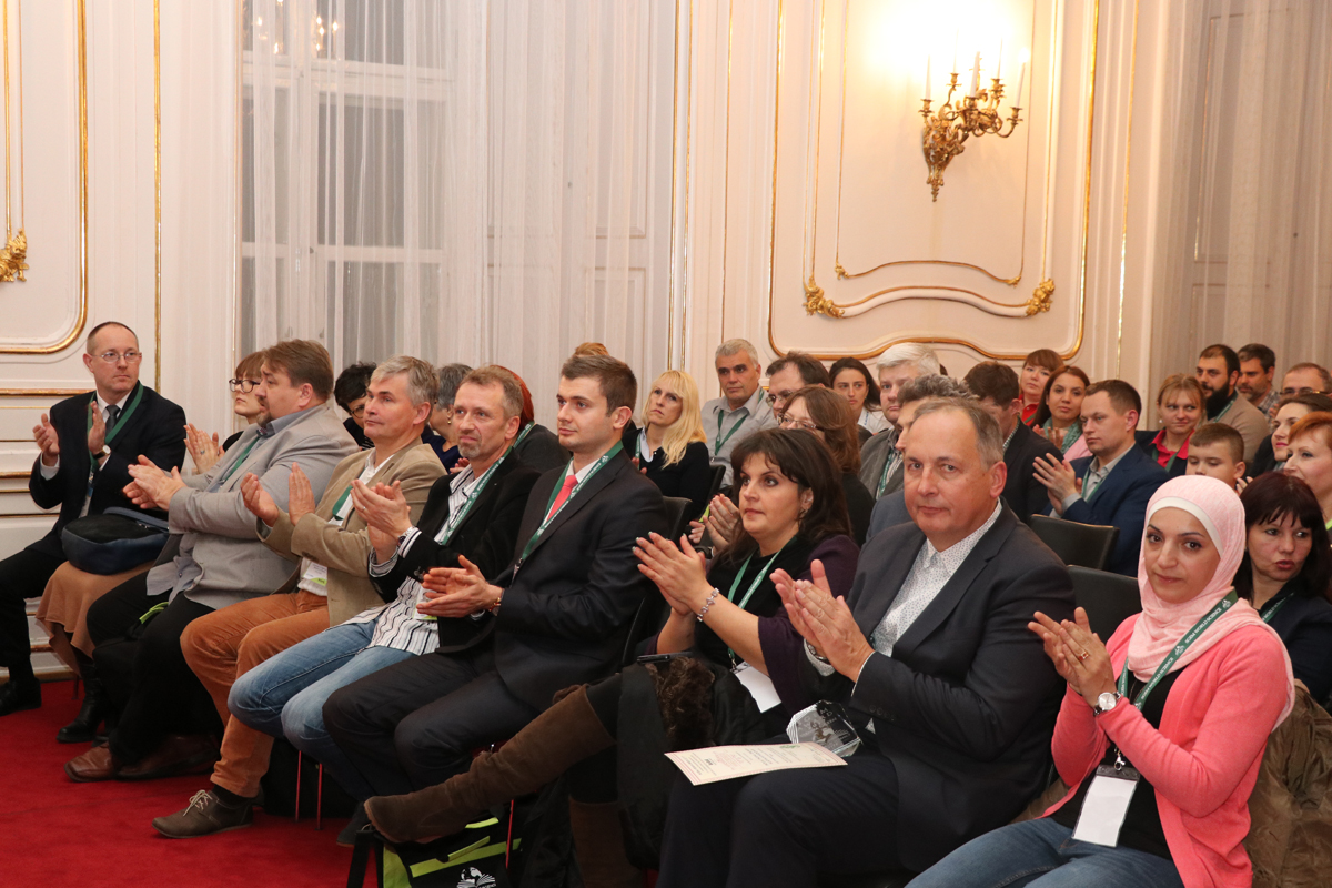 Miembros del público aplaudiendo en una sala de conferencias ornamentada