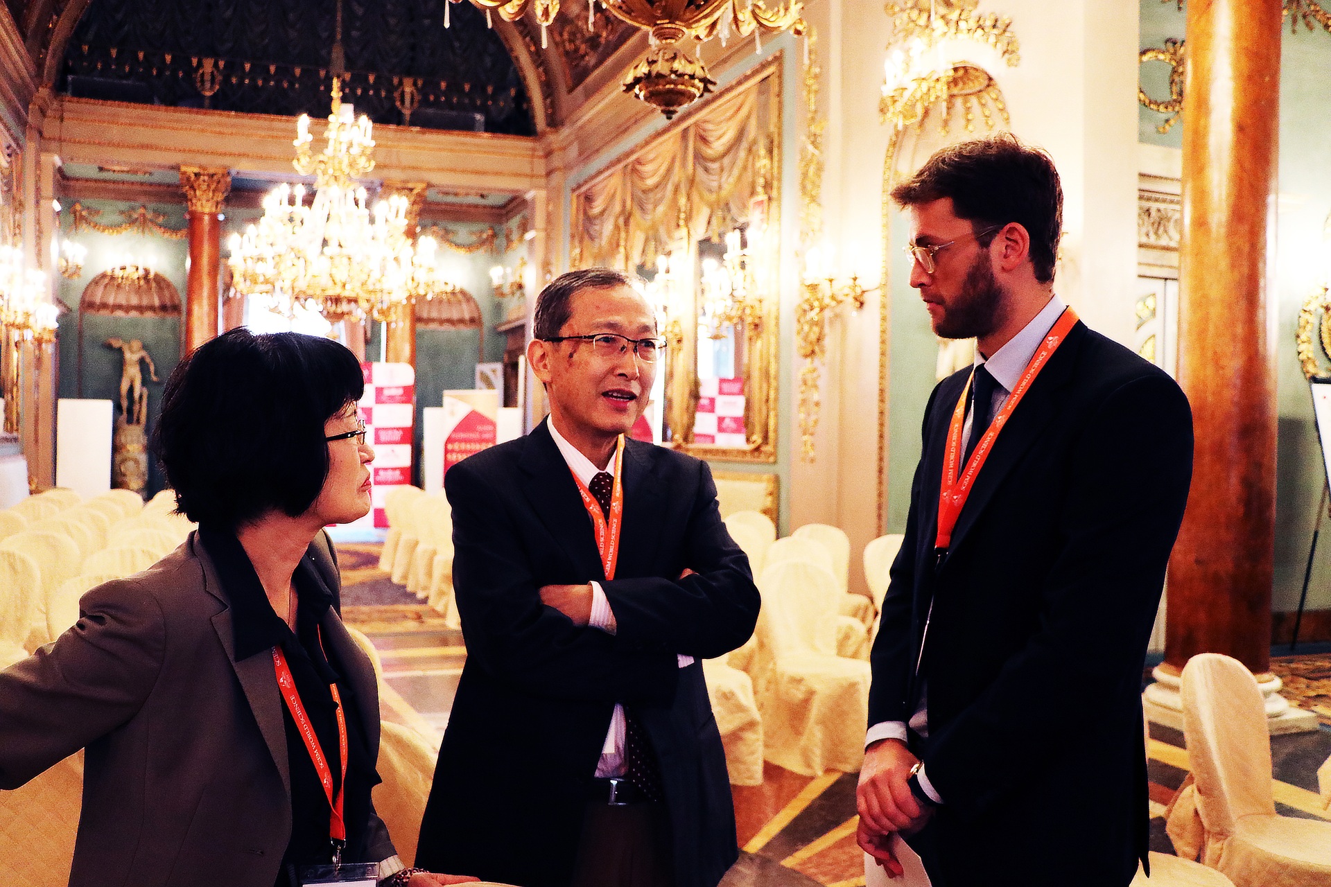 Tres delegados conversando entre sesiones en un recinto de conferencias ornamentado