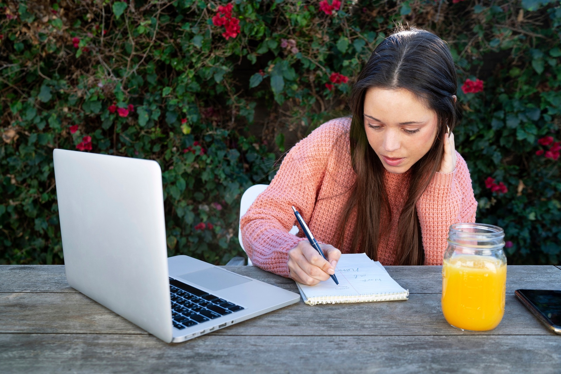A student writing notes beside a laptop outdoors