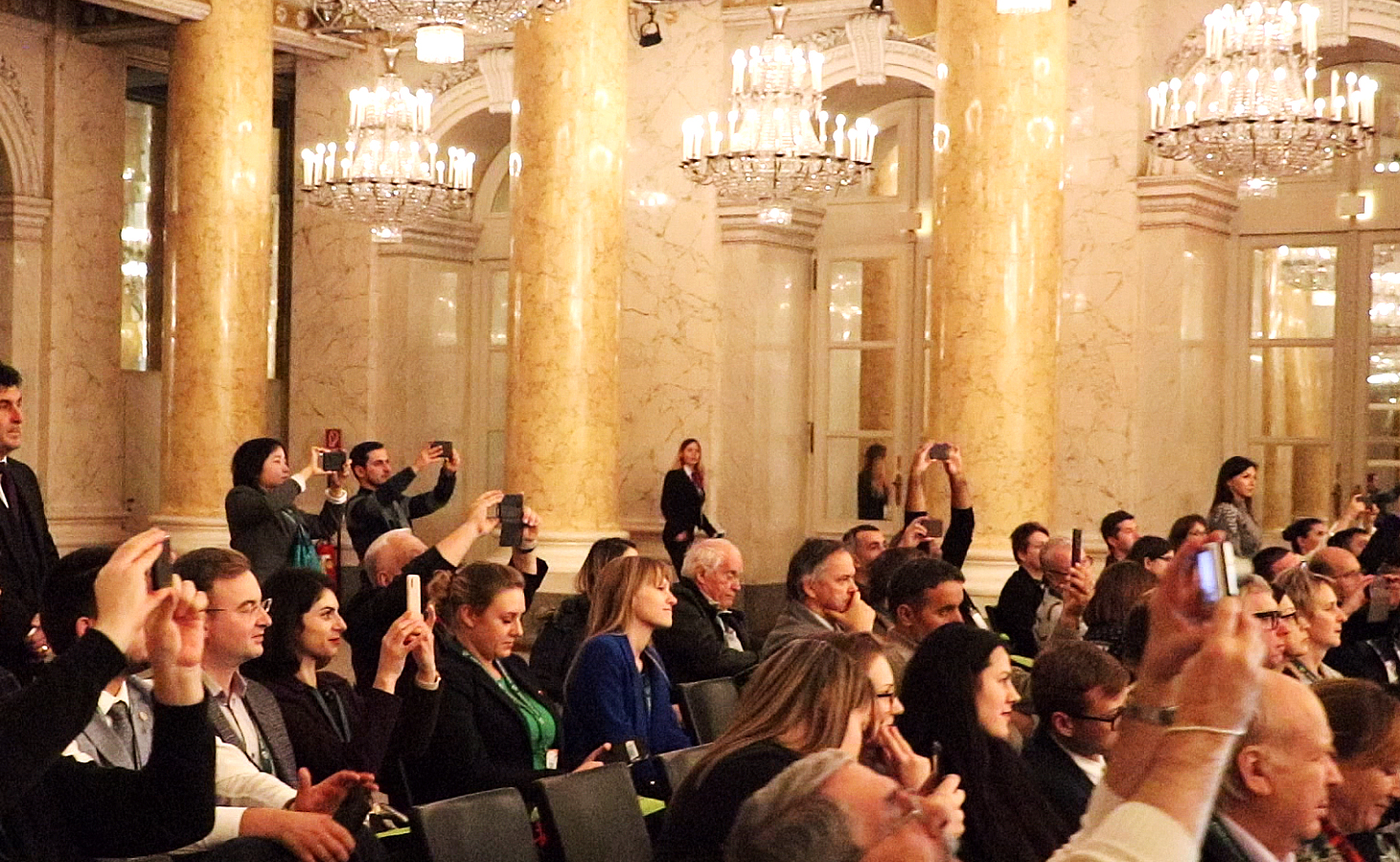 Conference delegates applauding in a chandelier-lit hall