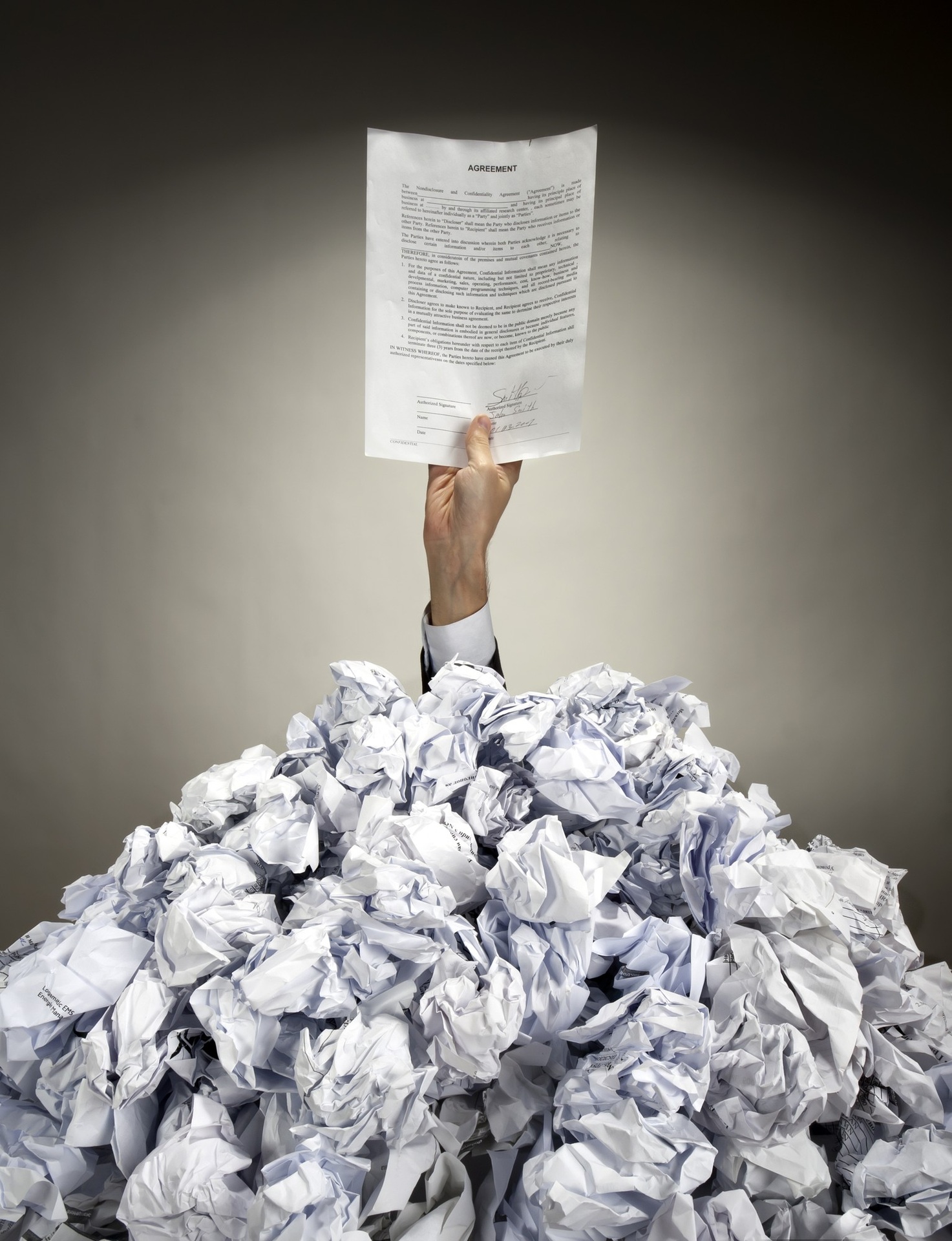 A hand holding a document above a pile of crumpled papers