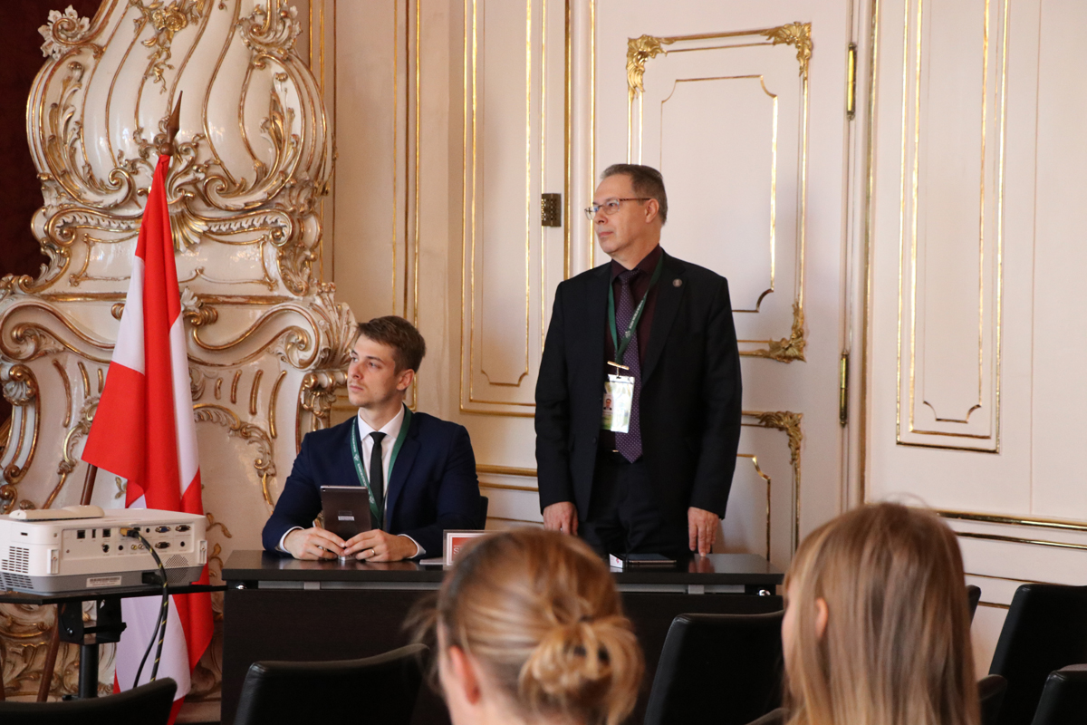A speaker addressing delegates beside a conference panel table