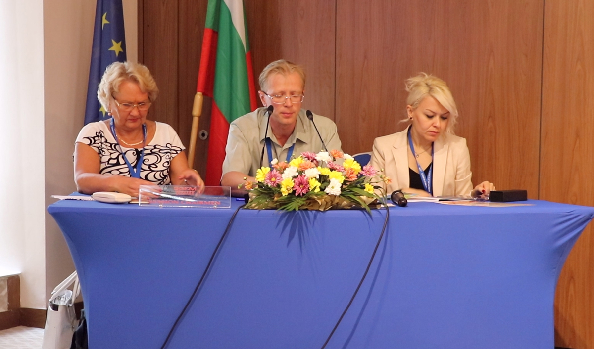 Three scientific session chairs seated behind flowers at a conference table