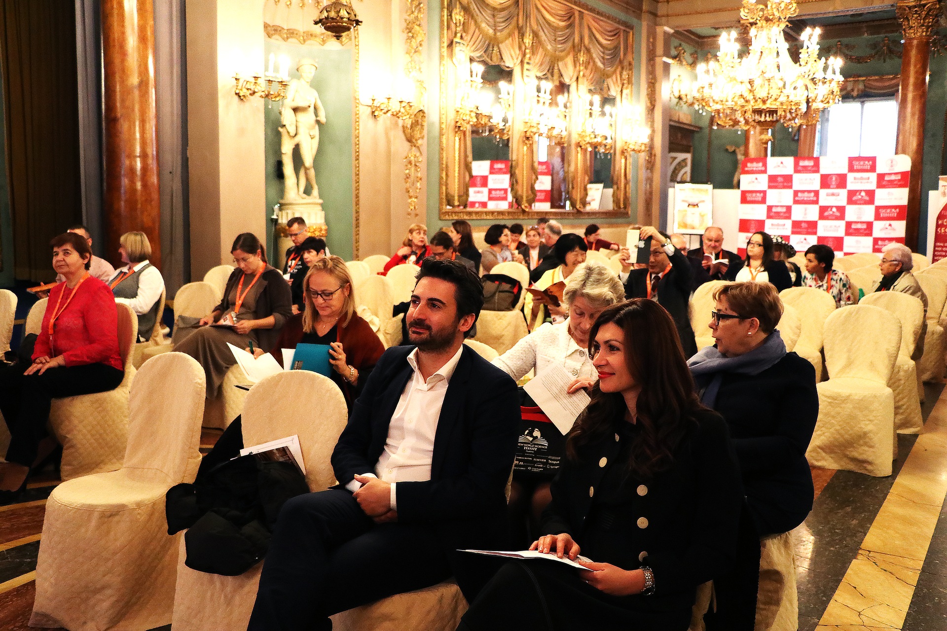 Delegates seated in a chandelier-lit conference hall