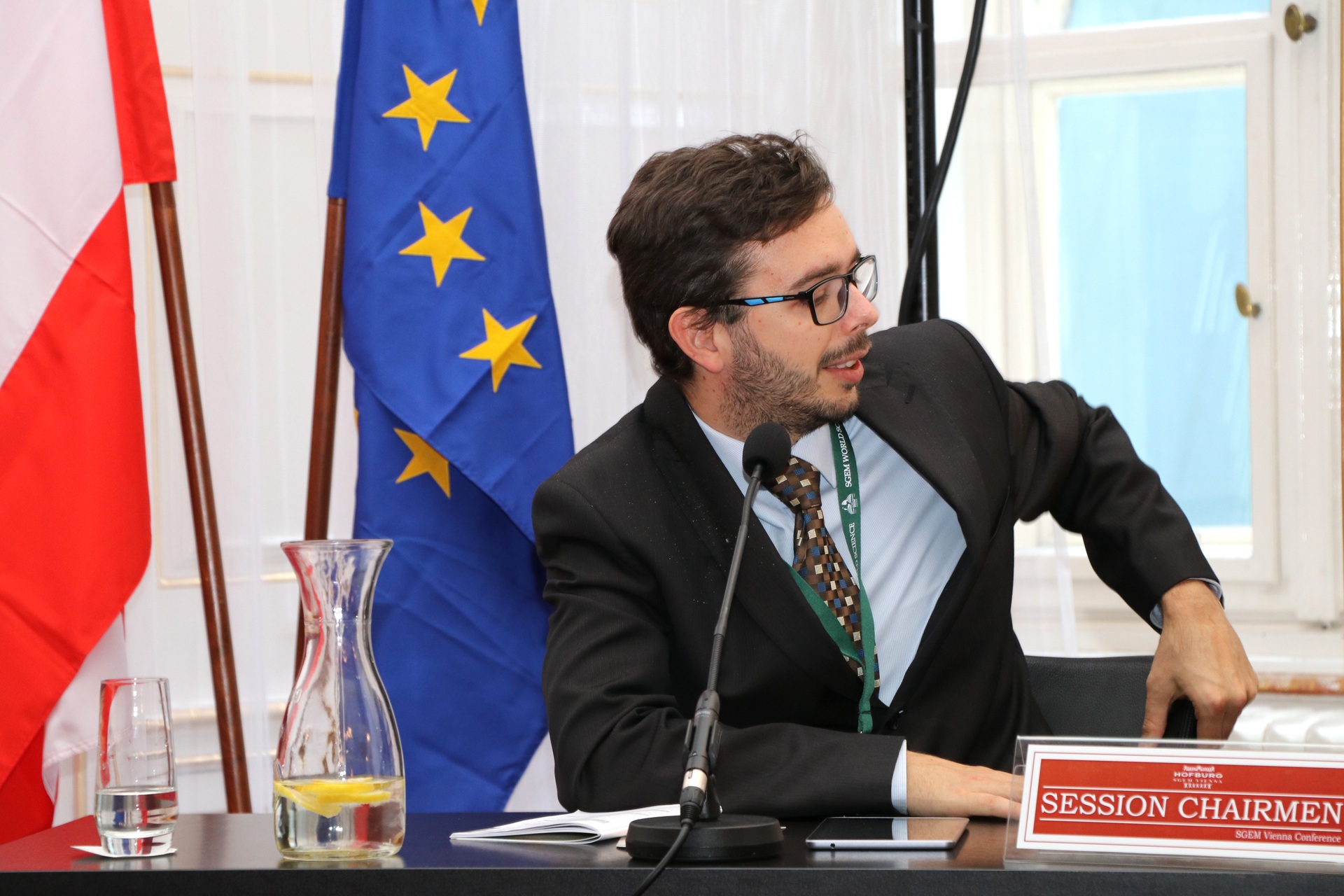 A session chair speaking beside Austrian and European Union flags