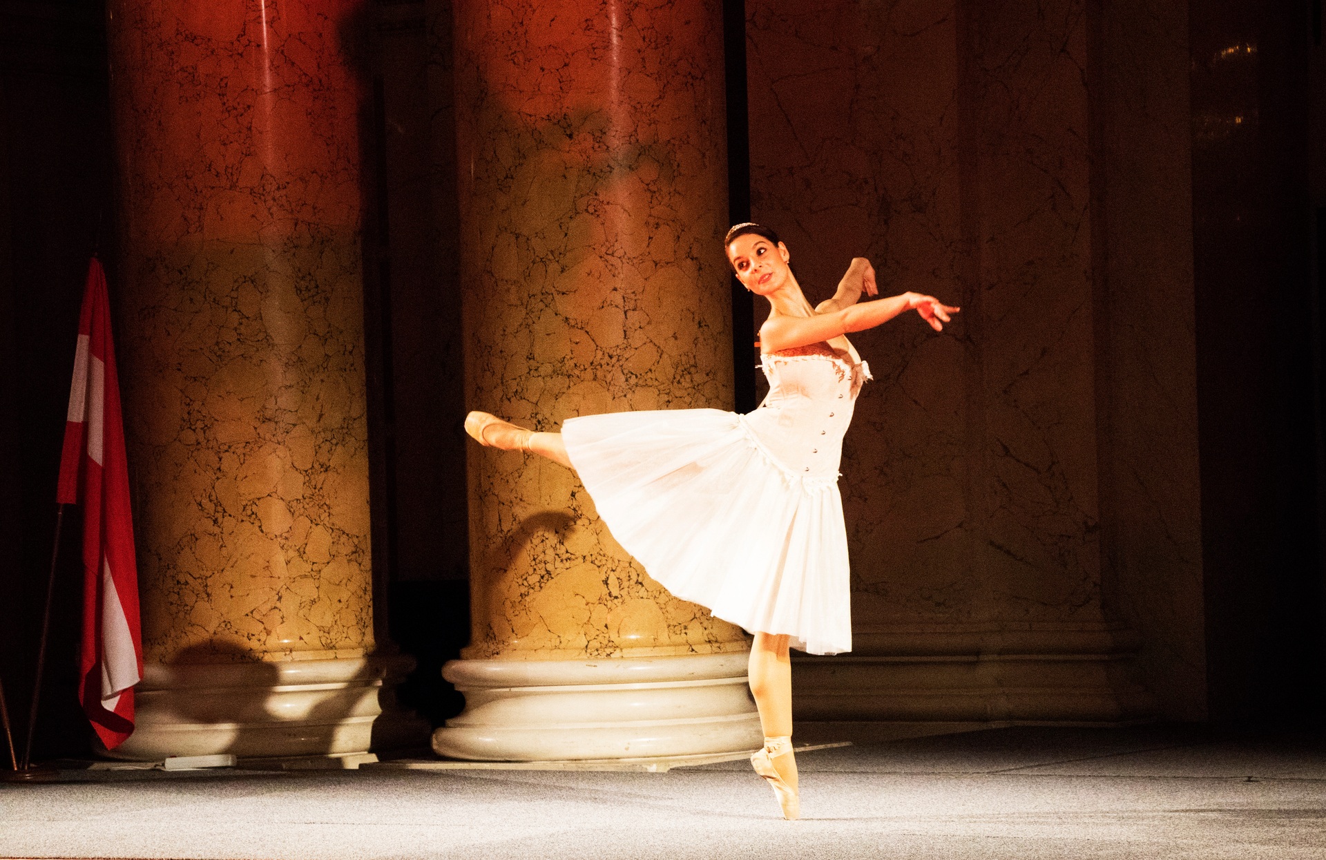 A ballerina performing in a white dress between marble columns