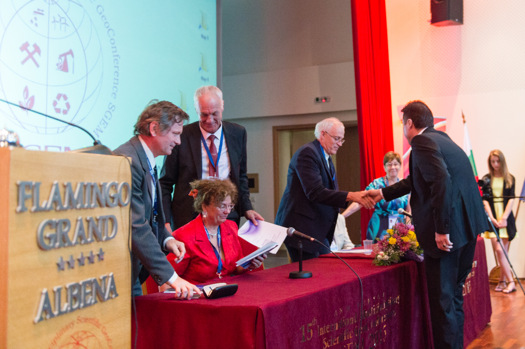 Delegates greeting each other at a conference panel table in Albena