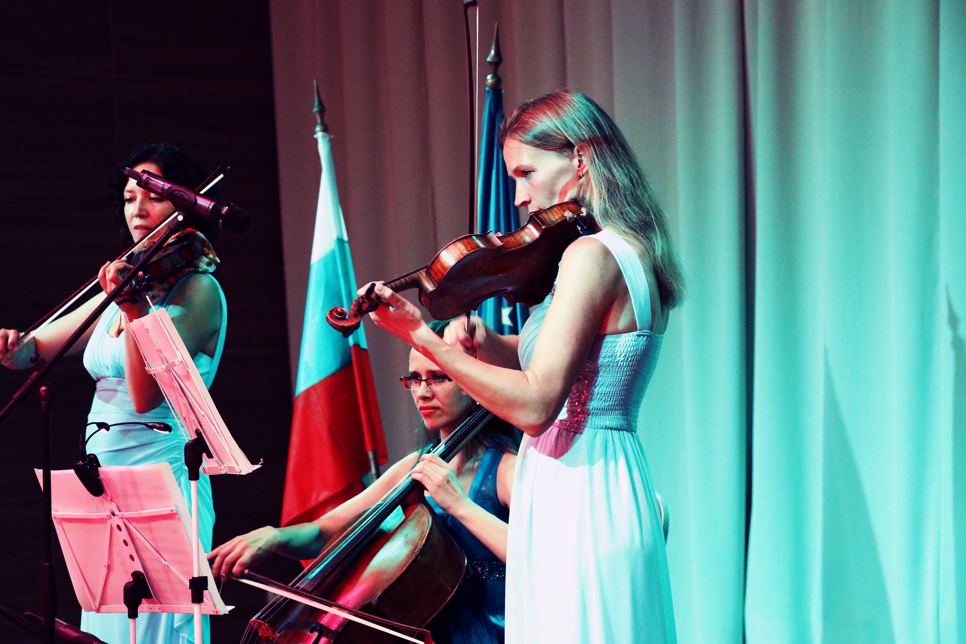 Violinists and a cellist performing under coloured stage lighting