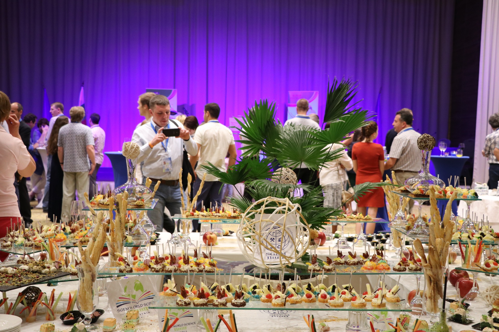 Guests mingling behind a decorated conference buffet under purple lighting