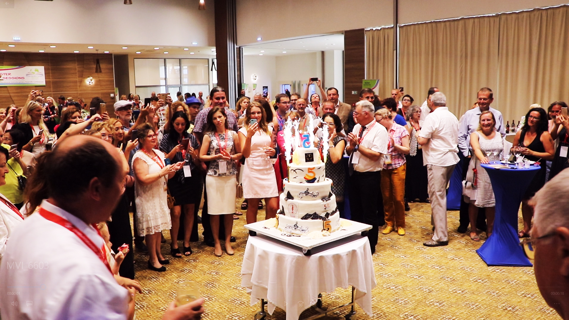 A speaker addressing conference guests beside a large cake