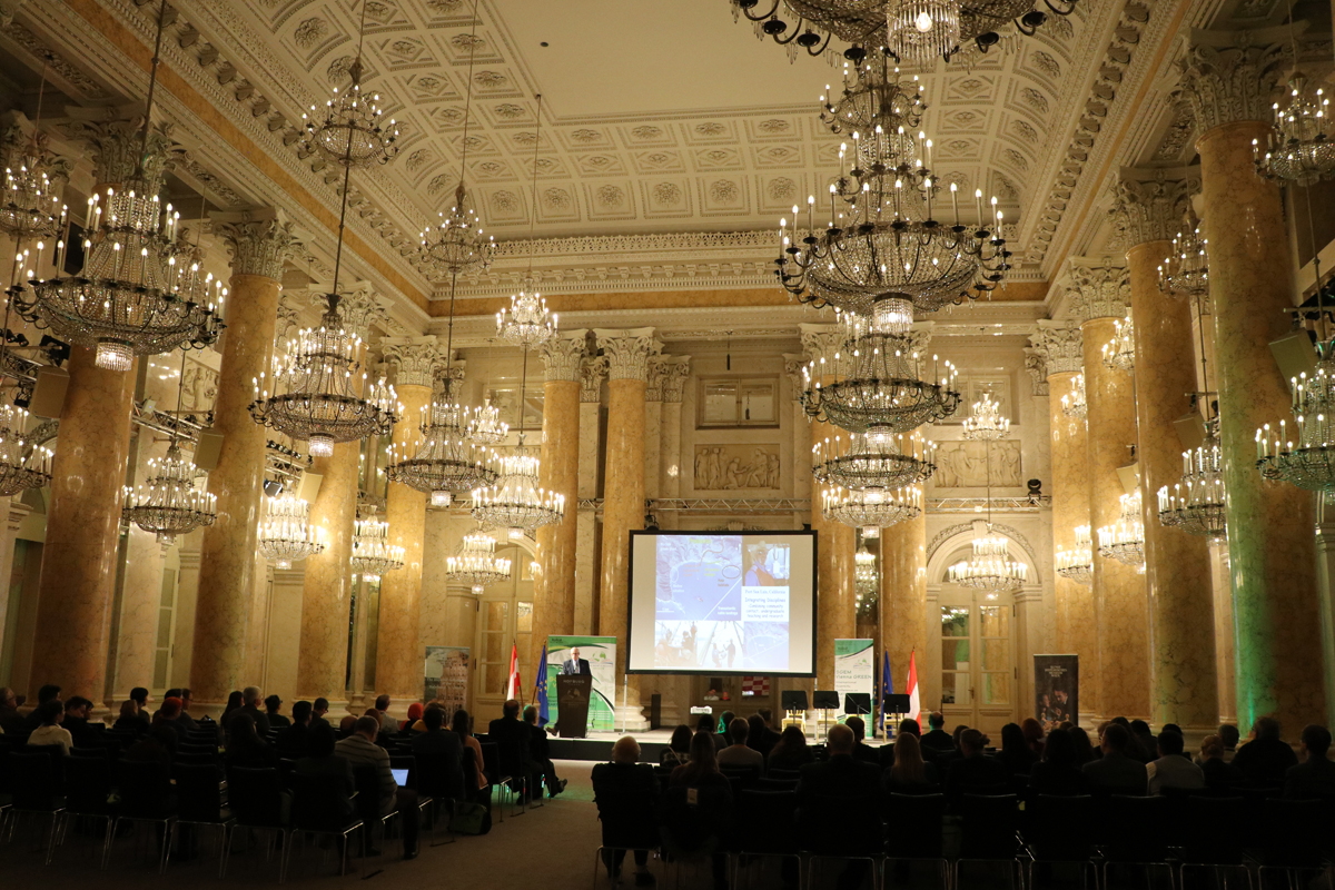 A full conference audience beneath gilded ceilings and chandeliers