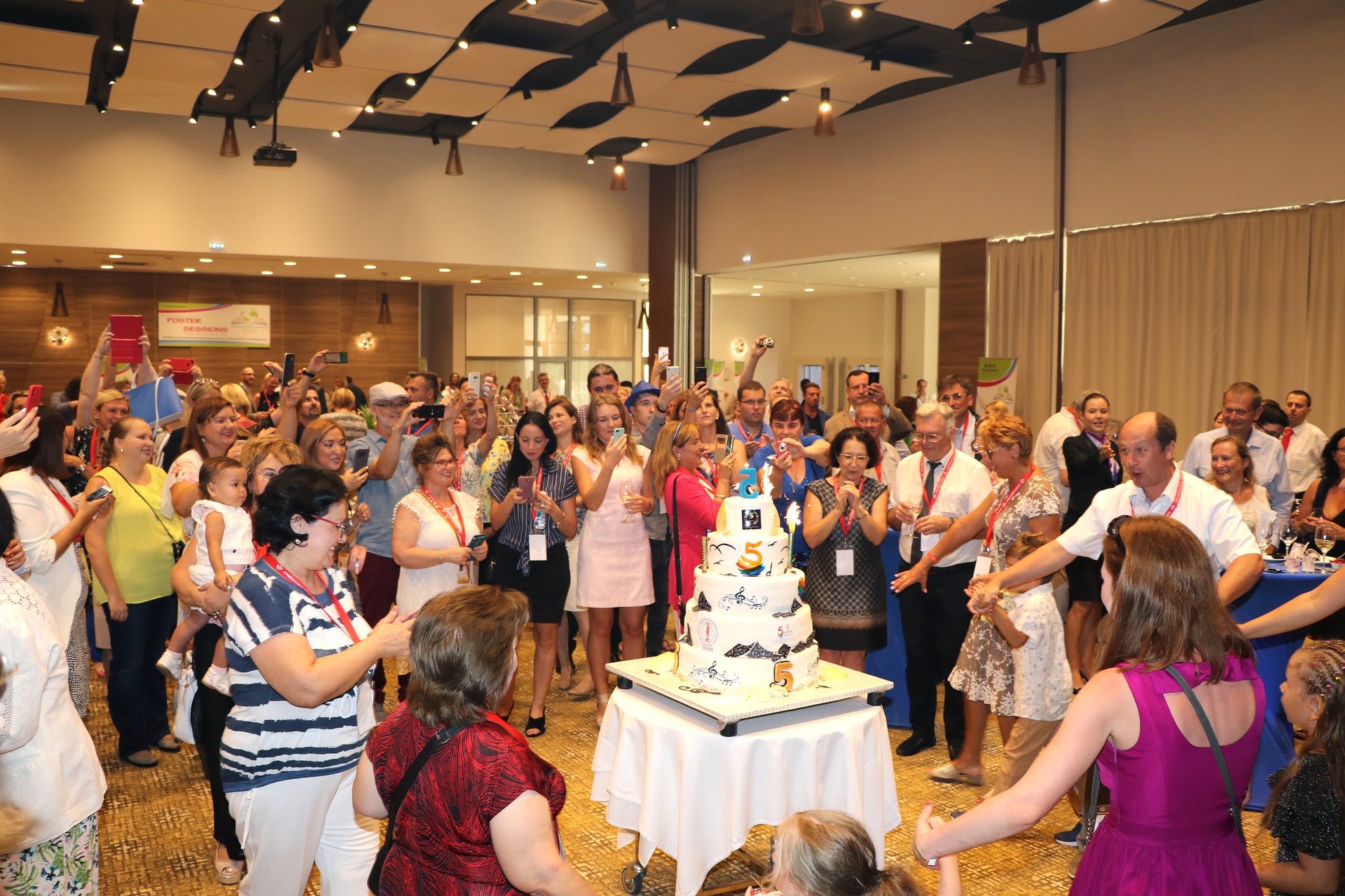 Participants applauding around a tiered conference celebration cake