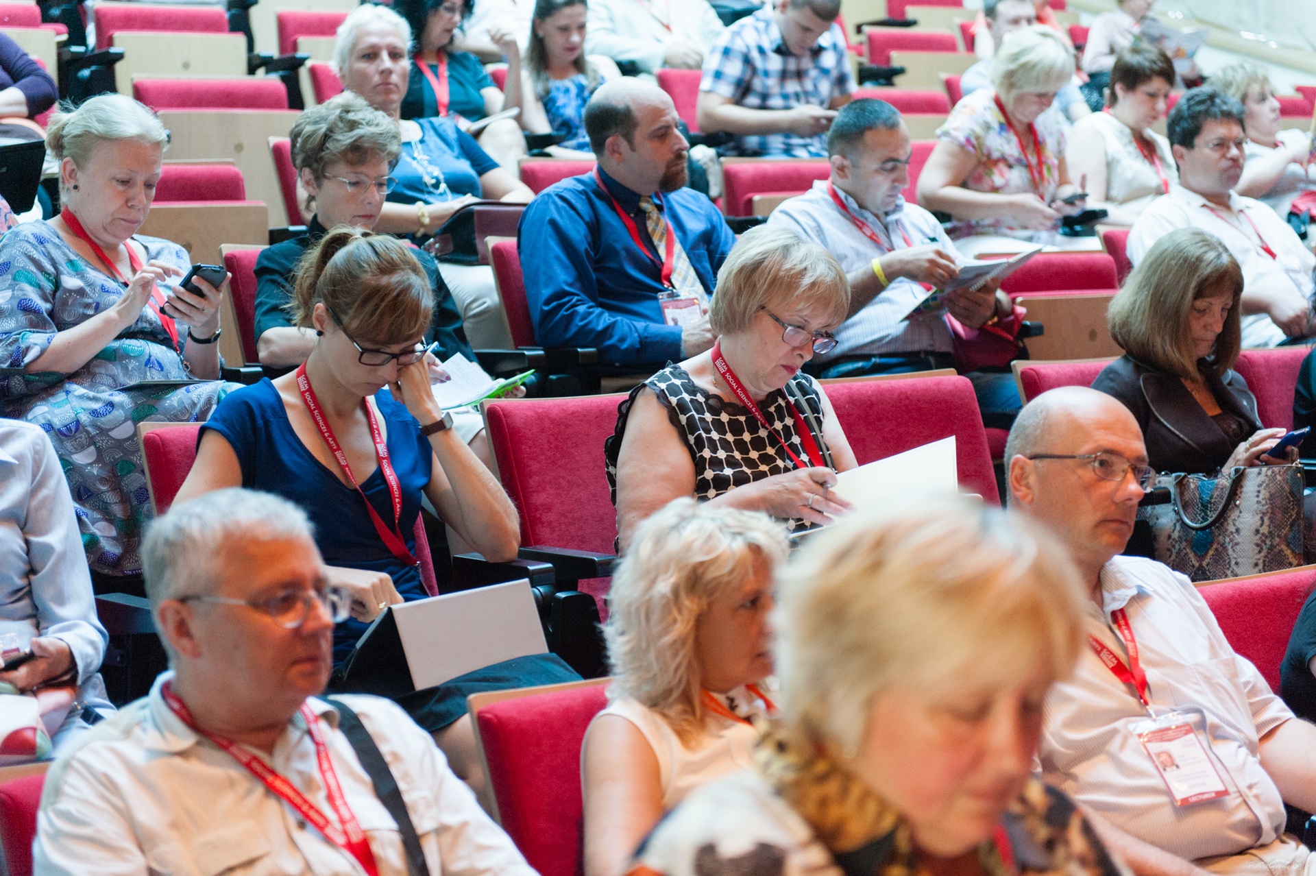 Conference participants reading notes and programmes in red seats