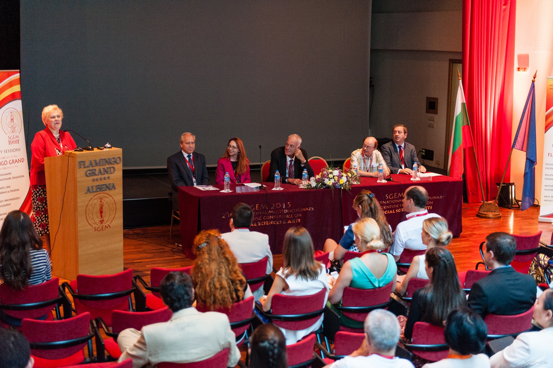 A speaker at a lectern beside a scientific conference panel