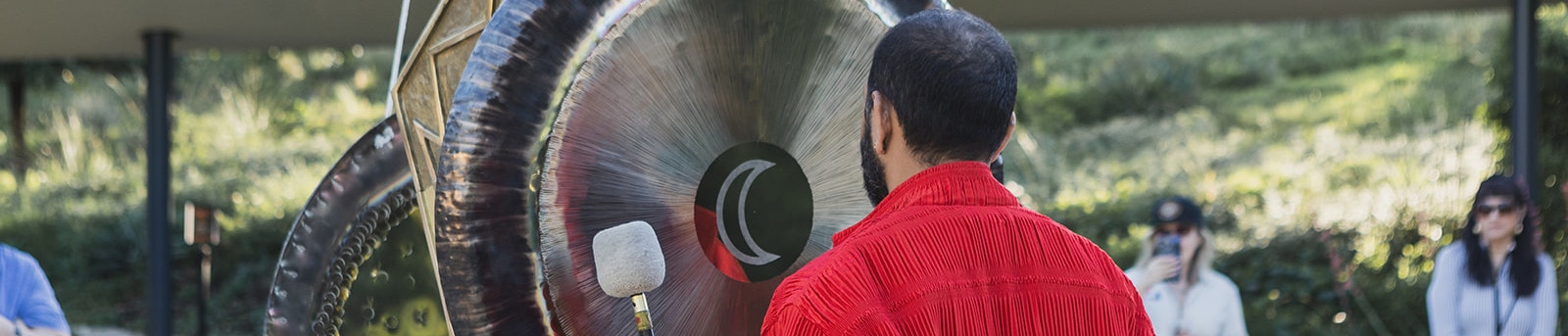 A performer standing beside a large gong outdoors